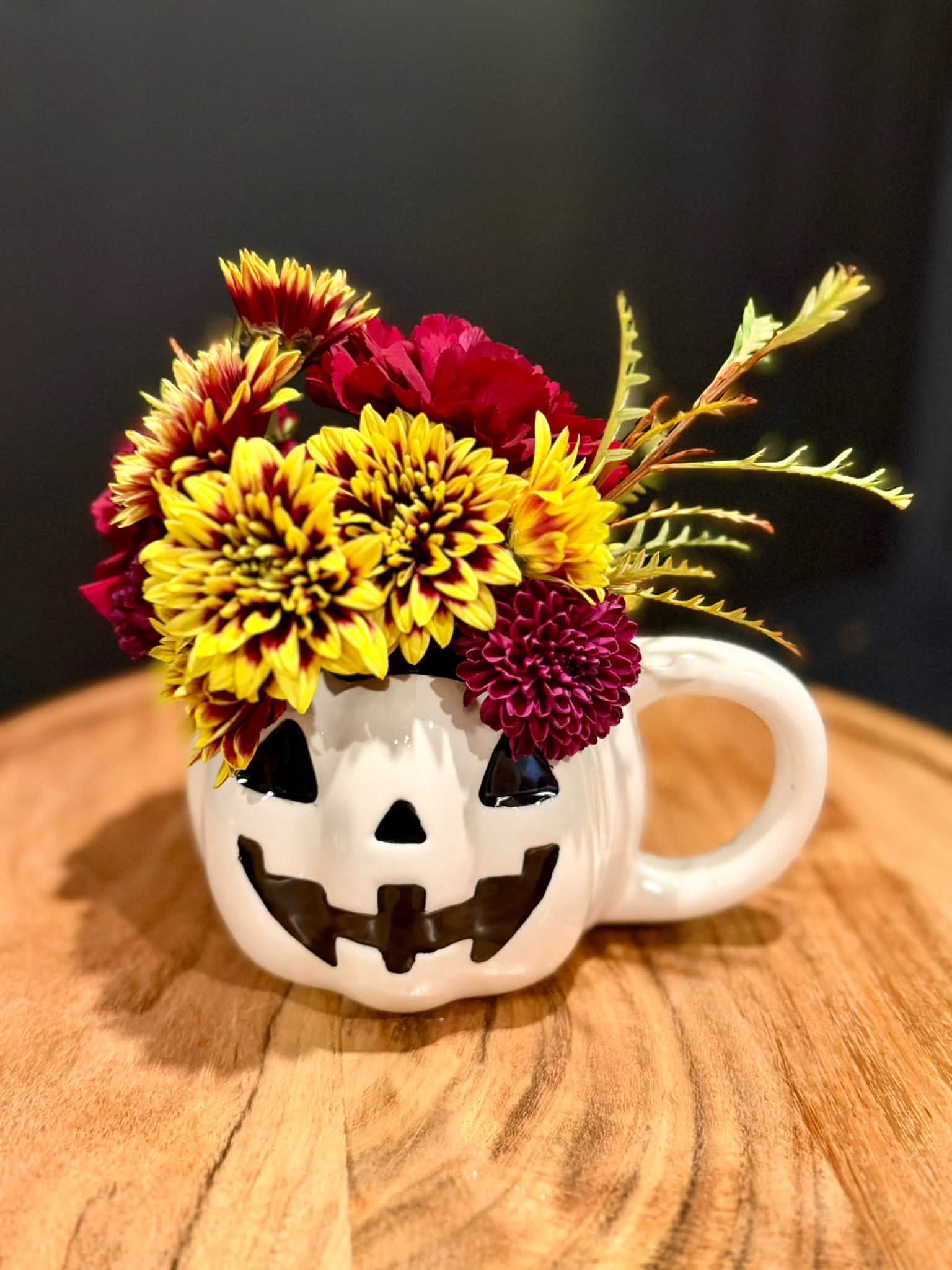 Yellow and burgundy flowers in a pumpkin mug
